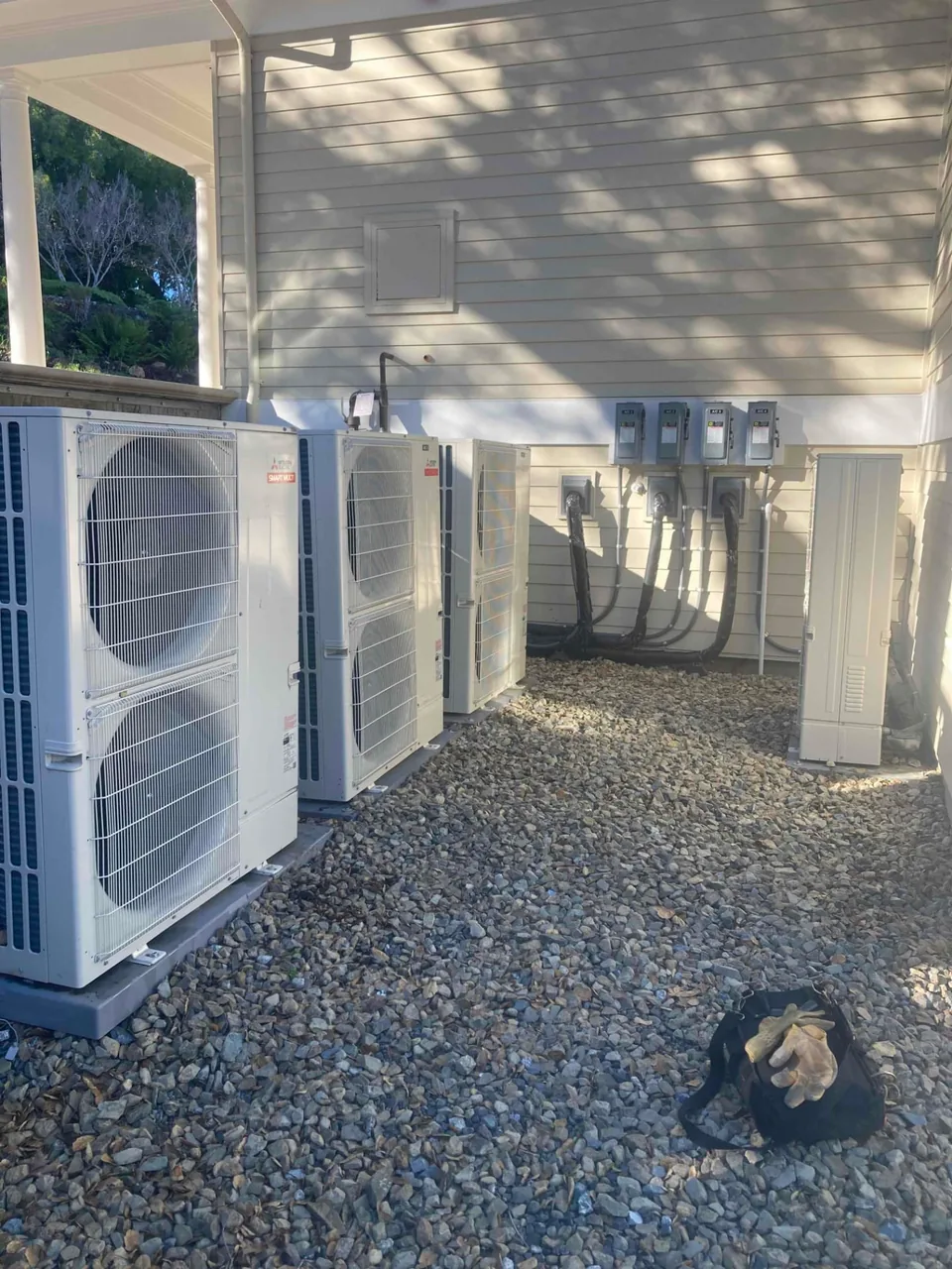 Mitsubishi outdoor heat pump units and electrical disconnects alongside a single-family home in Atherton CA 94027