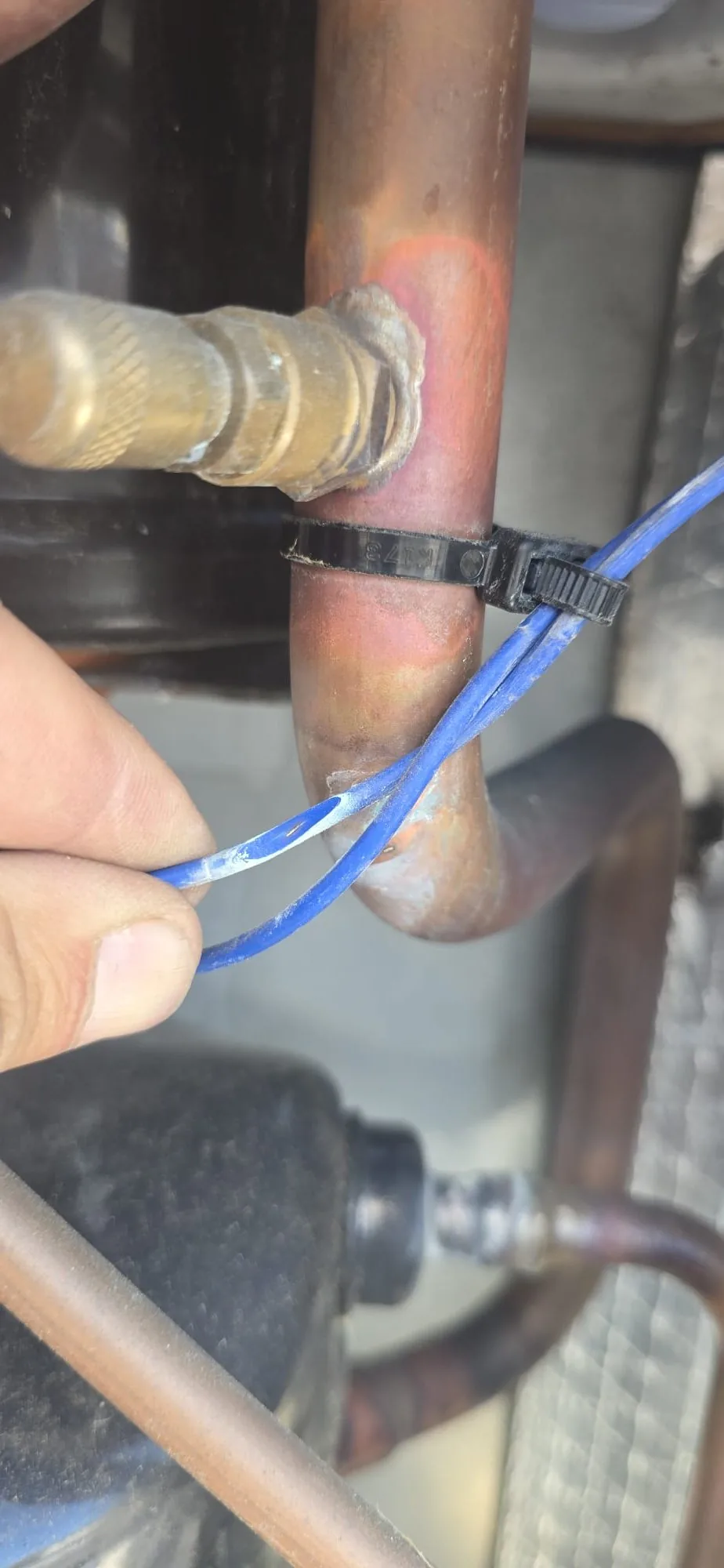 Low-voltage wire held next to a copper refrigerant line on a rooftop package unit