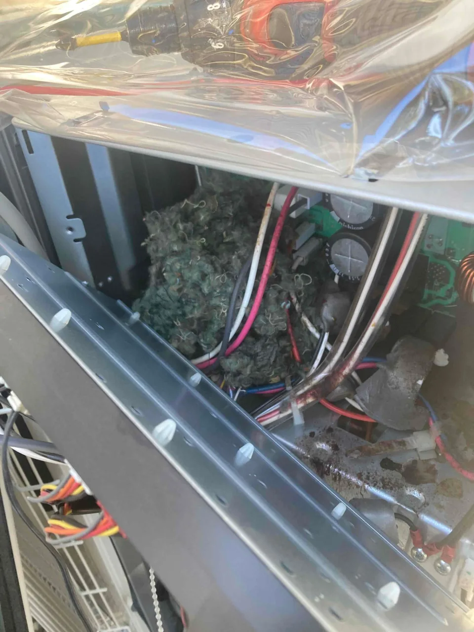 Nesting material and debris inside an opened heat pump unit beside its wiring and circuit board in Atherton CA 94027