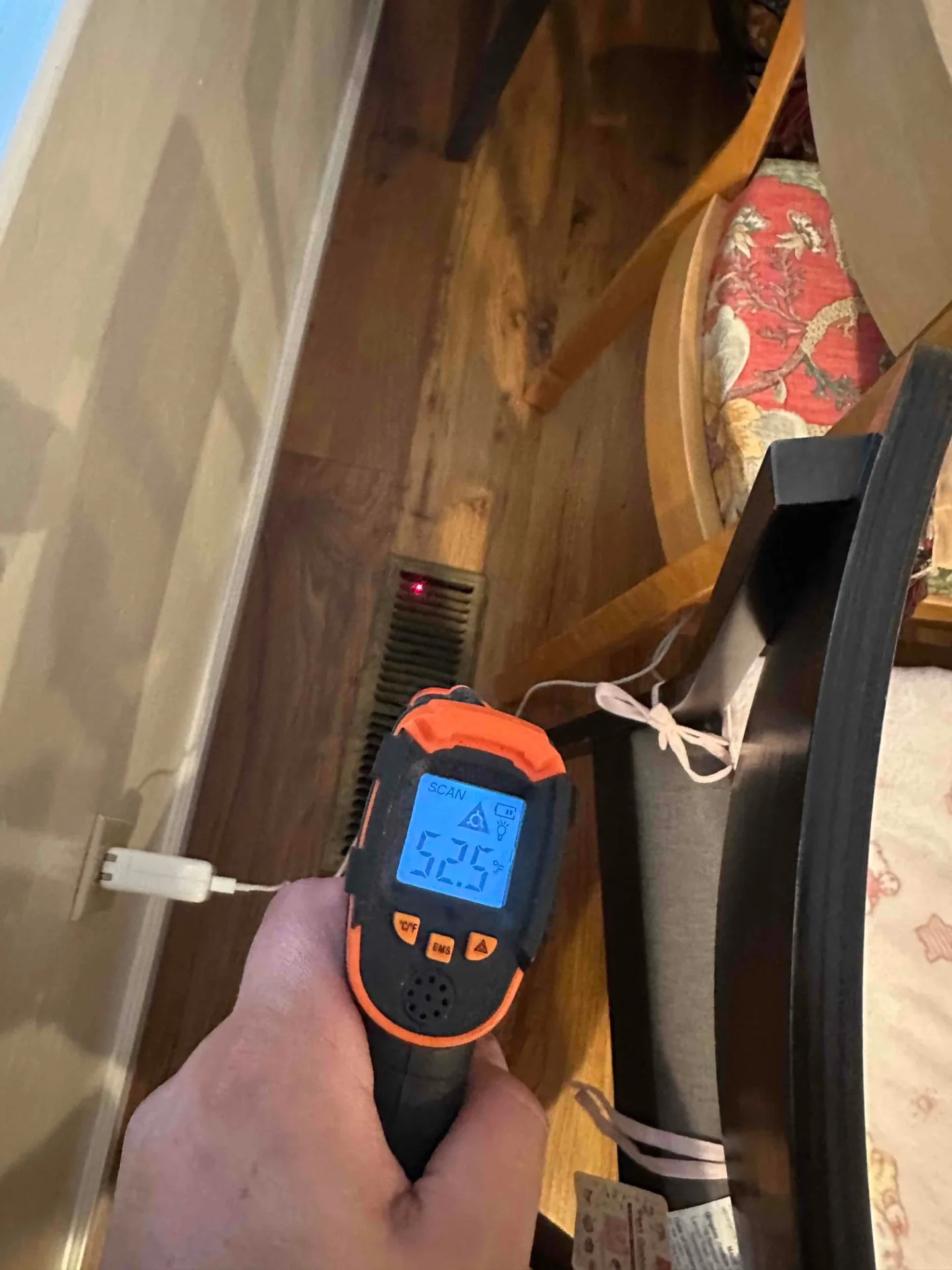 Handheld temperature meter aimed near a floor register
