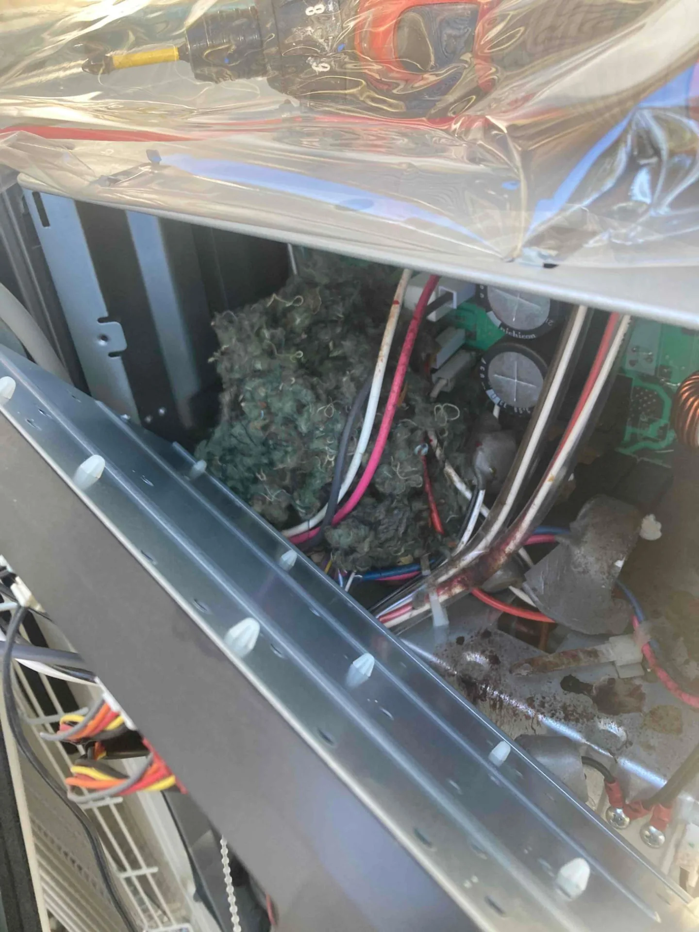 Nesting material and debris inside an opened heat pump unit beside its wiring and circuit board in Atherton CA 94027