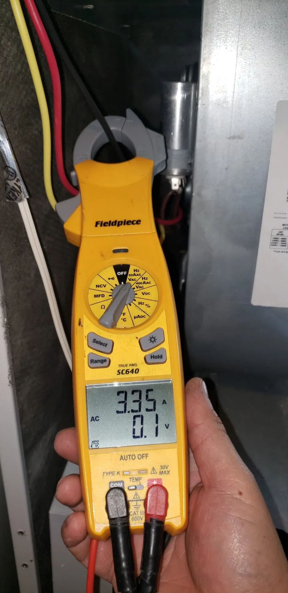 Clamp meter displaying an electrical reading beside indoor heat pump equipment