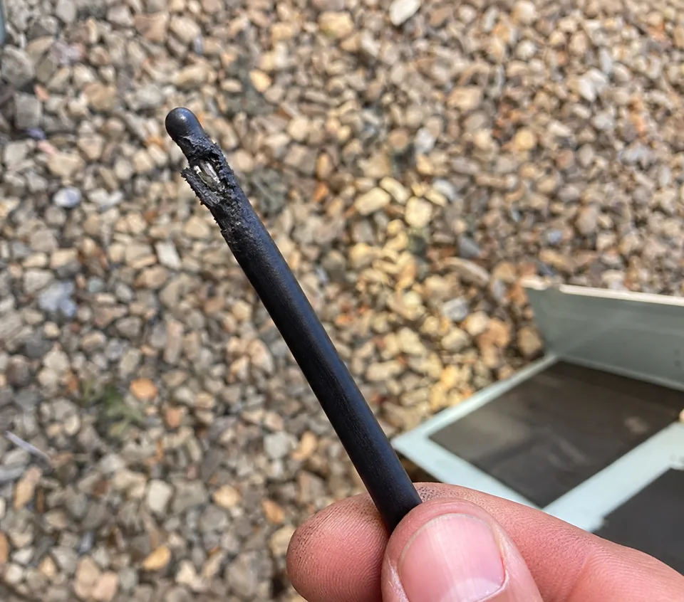 Close-up of a chewed wire end held in front of the outdoor heat pump equipment in Atherton CA 94027