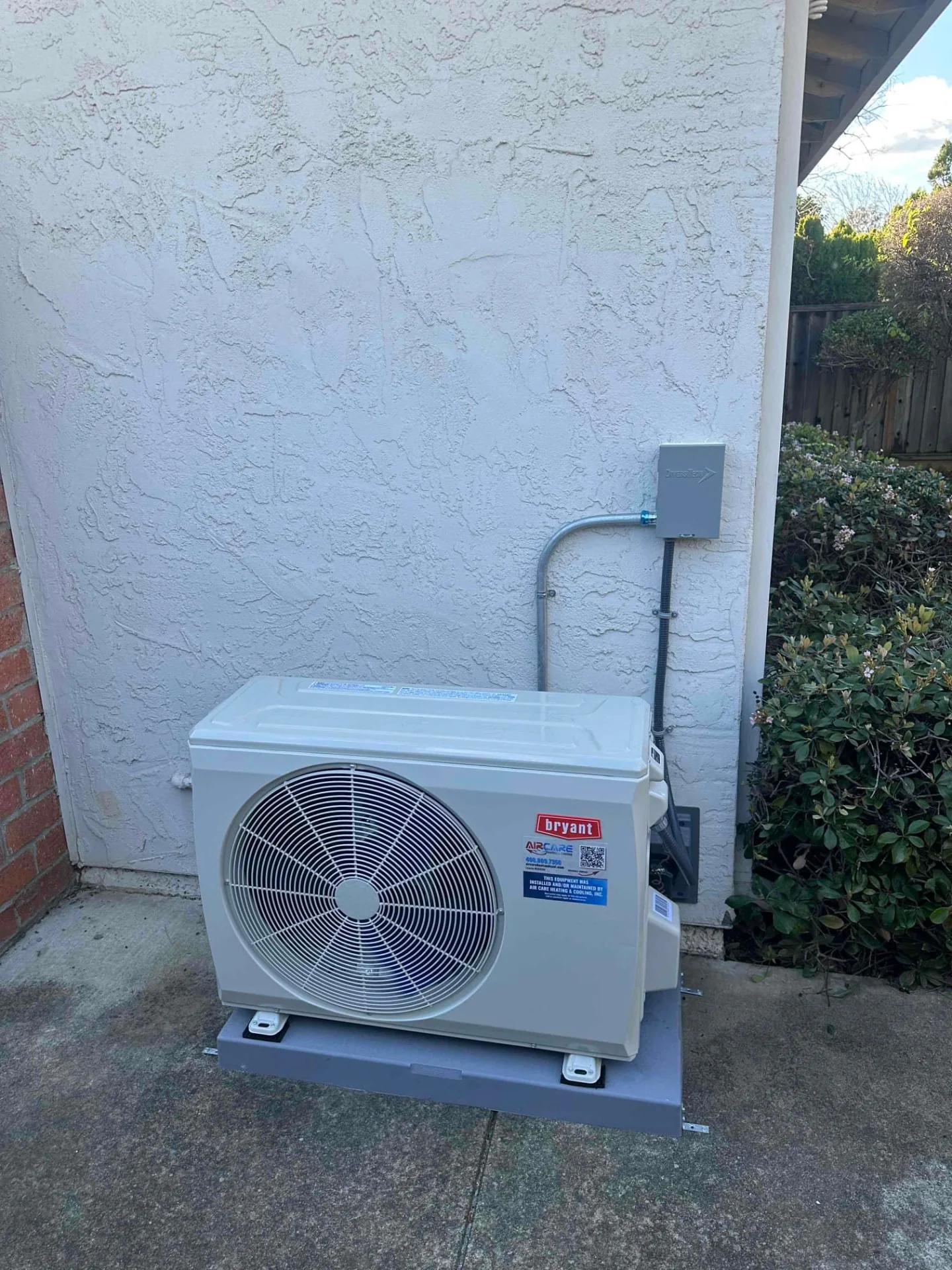 Bryant outdoor heat-pump unit beside a stucco wall and shrubs