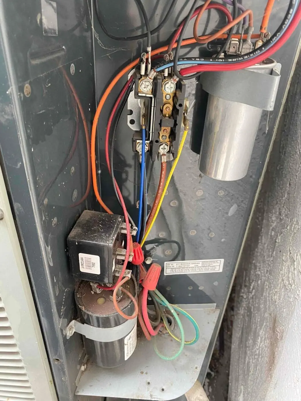 Open electrical compartment of an outdoor air conditioning unit showing the contactor, capacitor, and wiring
